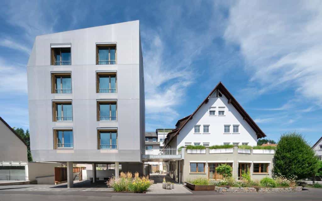 Modern hotel next to traditional white building under blue sky in Constance.