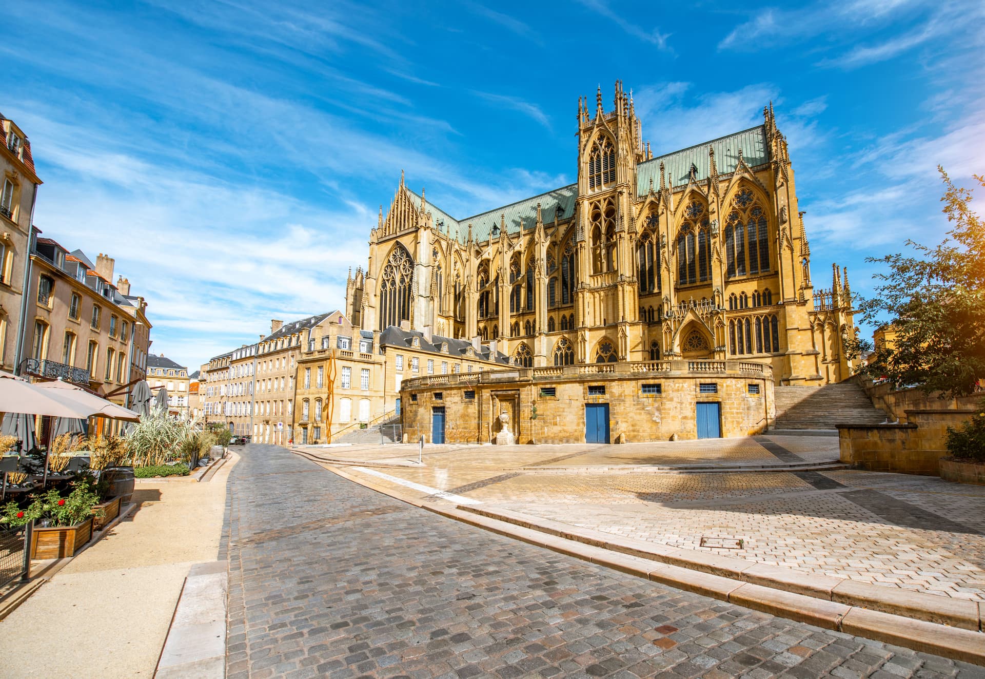 Gothic cathedral facade next to cobblestone square and historic buildings in Metz, France.