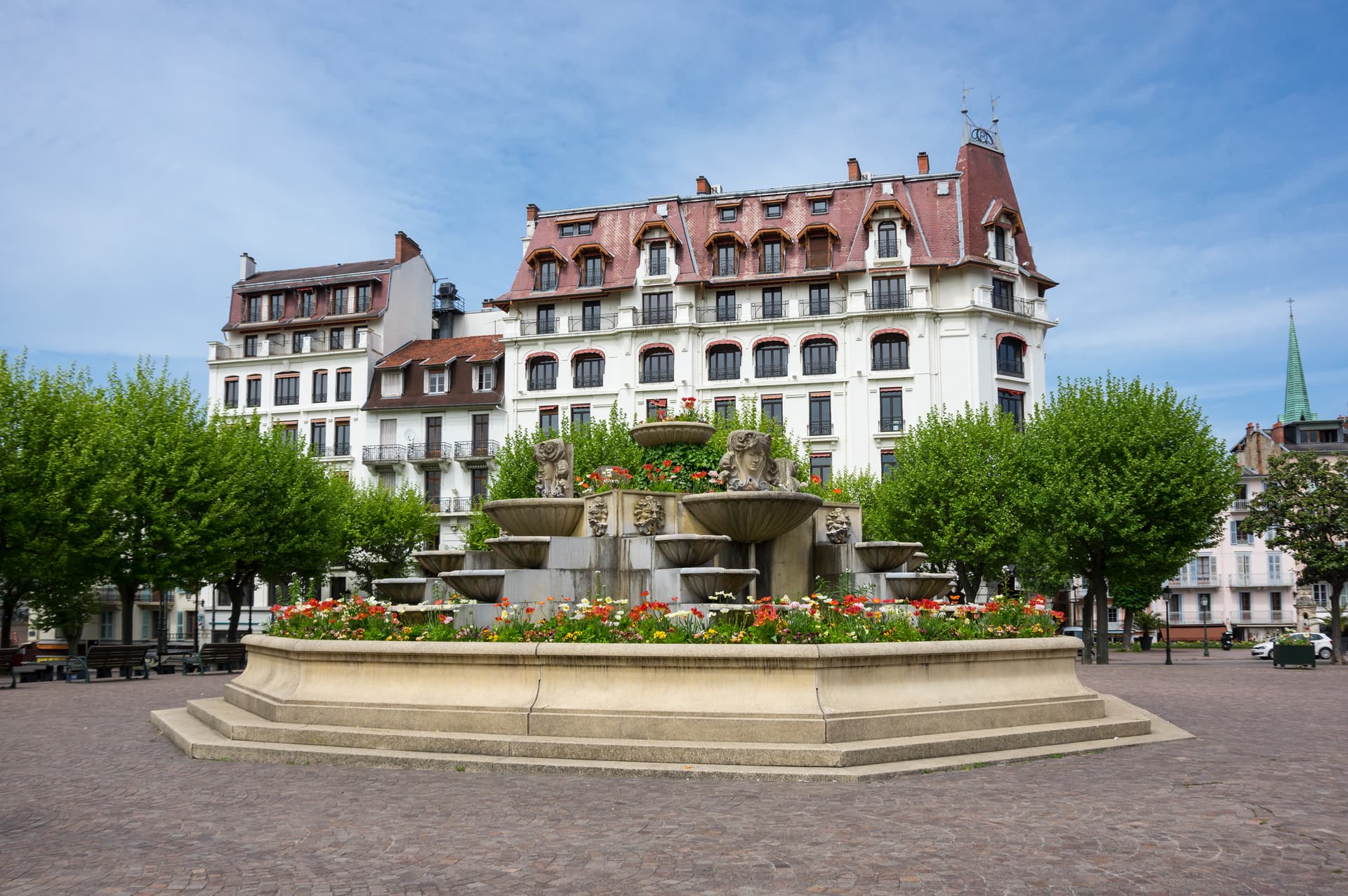 Tiered stone fountain with carved faces and flowers in Aix-les-Bains square.