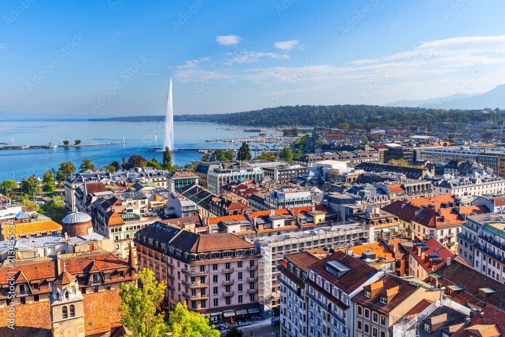 Aerial view of Geneva cityscape with Jet d'Eau fountain in Lake Geneva and mountains.