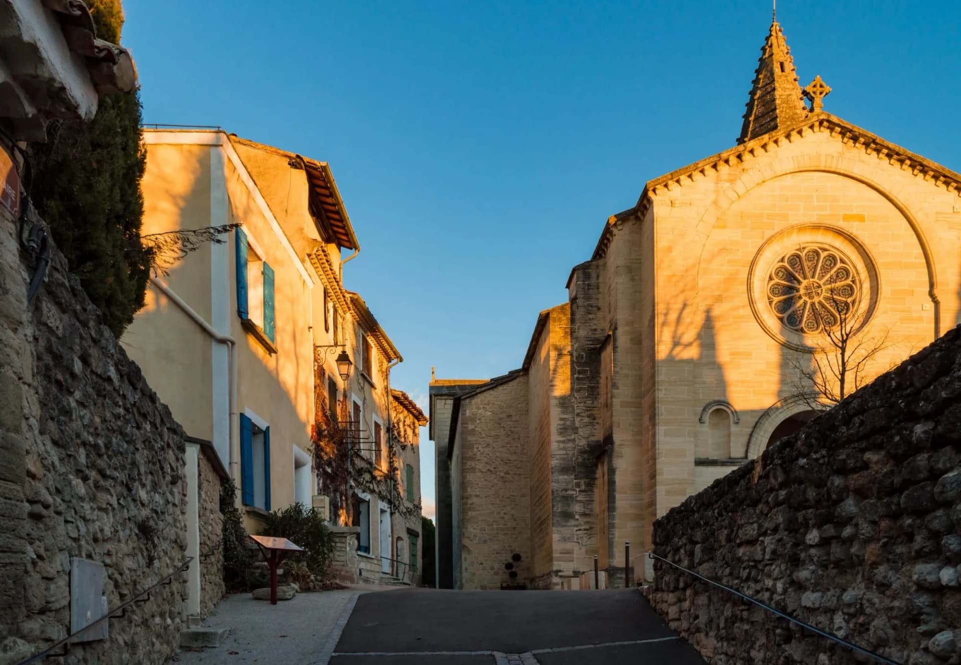Narrow street in Mazan leading uphill toward a stone church facade at sunset