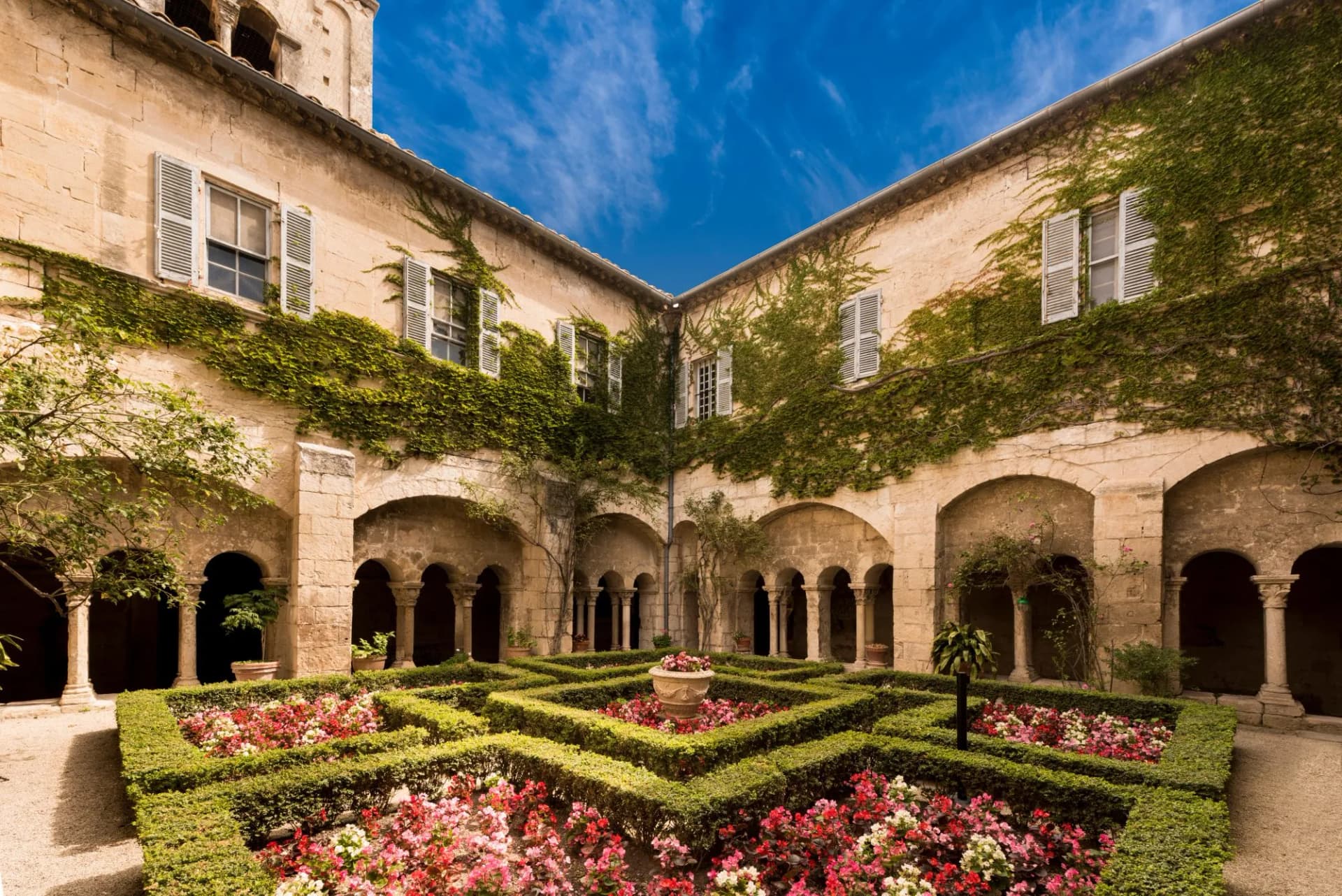 Courtyard garden with manicured hedges and flowers at San Paul de Mausole monastery under blue sky.