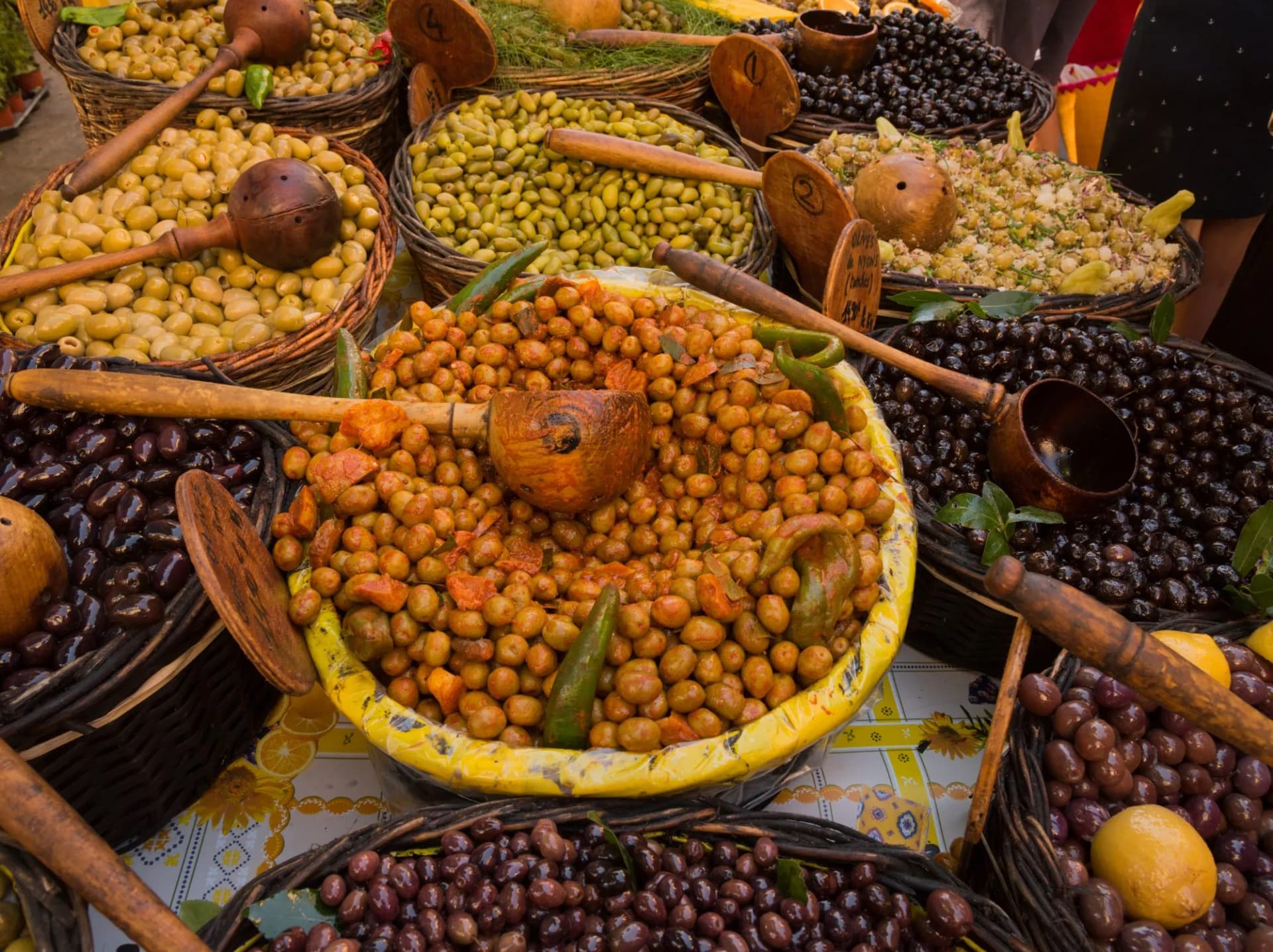 Various olives and preserved vegetables displayed in baskets with wooden scoops at a market in Saint-Remy-de-Provence.