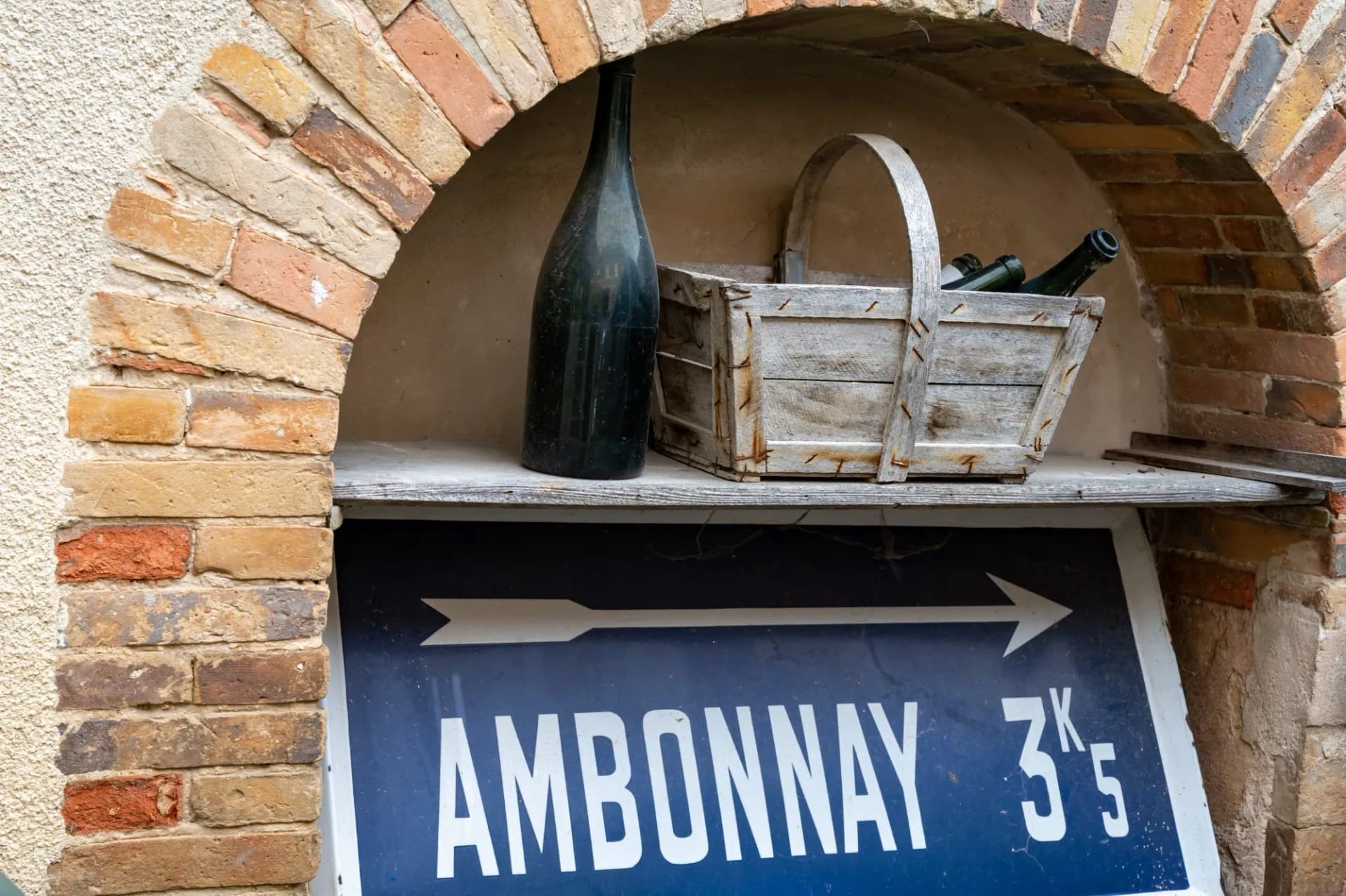 Ambonnay direction sign under brick arch with wine bottle and wooden basket