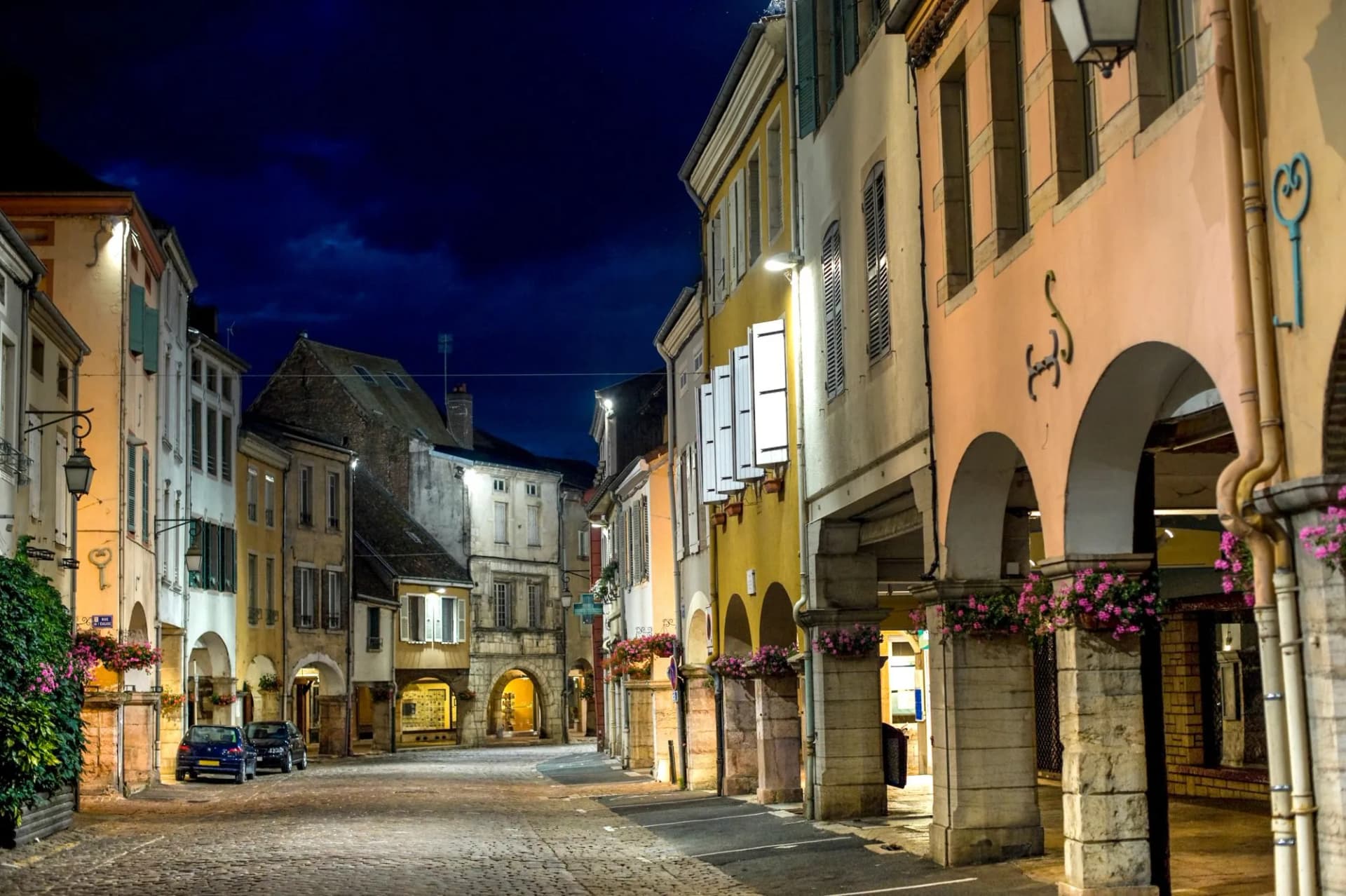 Cobblestone street in Louhans at night with illuminated historic buildings and covered arcades.