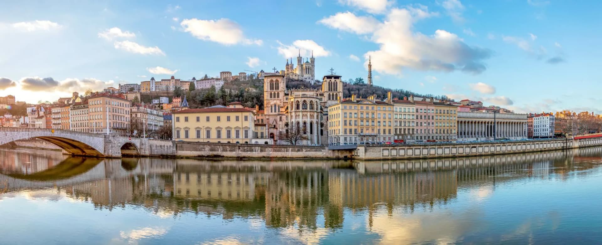 Cityscape along the Saône river with historic buildings and a bridge reflected in the water.