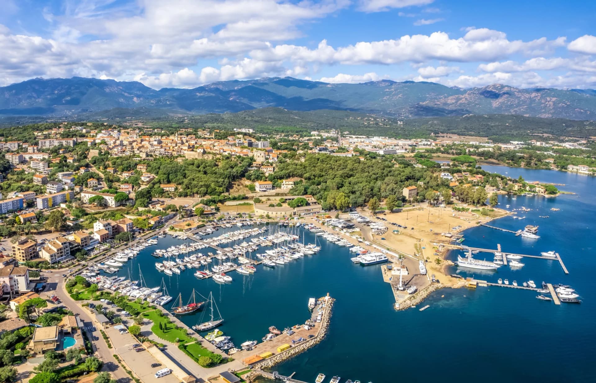 Aerial view of Porto Vecchio marina filled with boats, backed by a town and mountains.