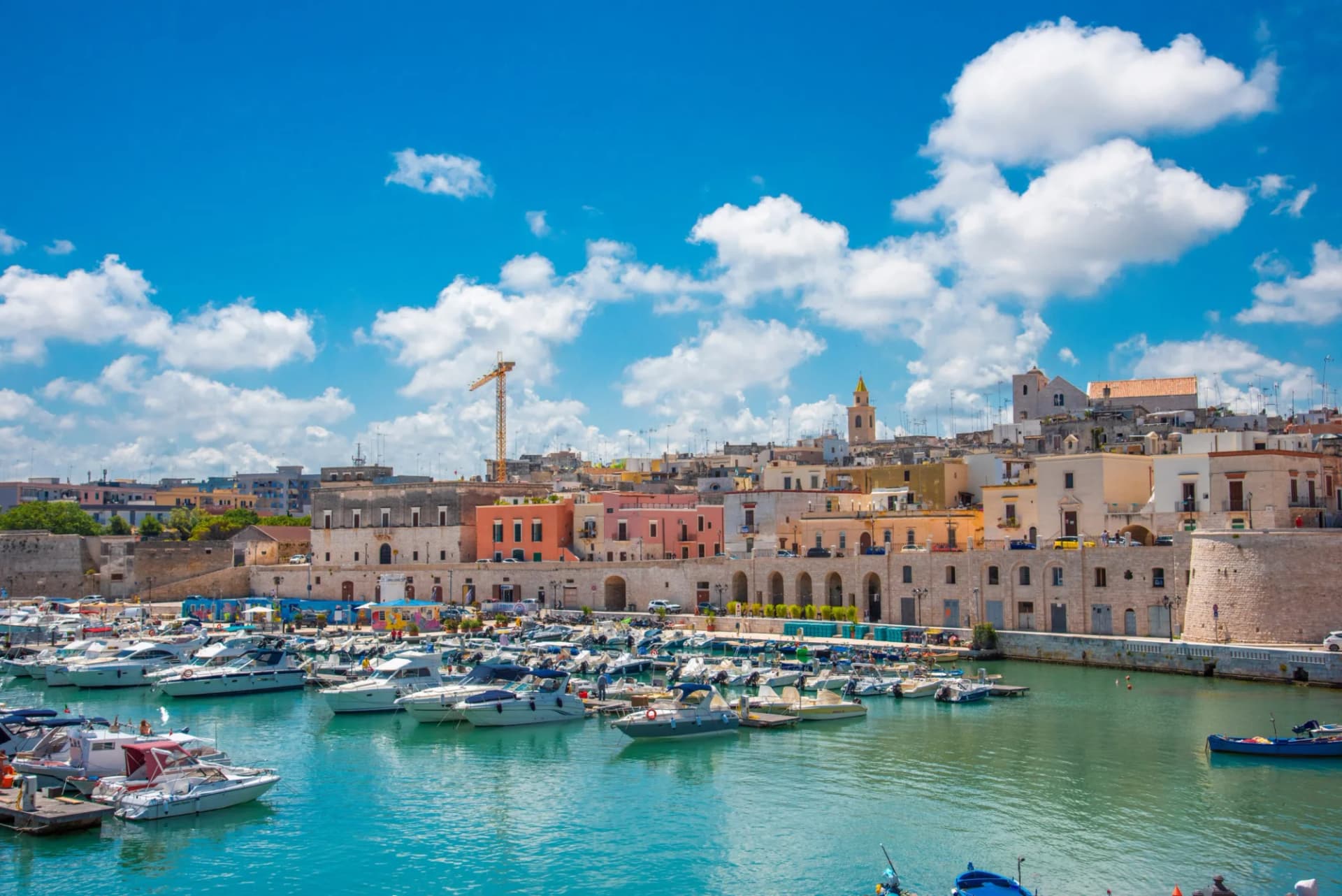 Boats docked in harbor with colorful coastal town buildings under bright blue sky.