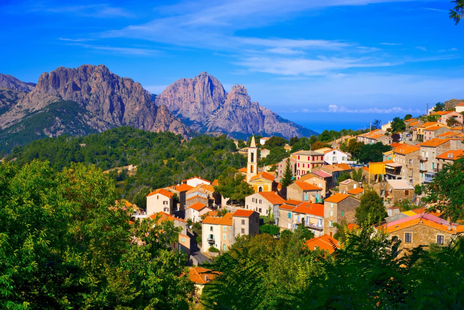 Village with terracotta roofs nestled below rugged mountains near the sea in Porto, Corsica.
