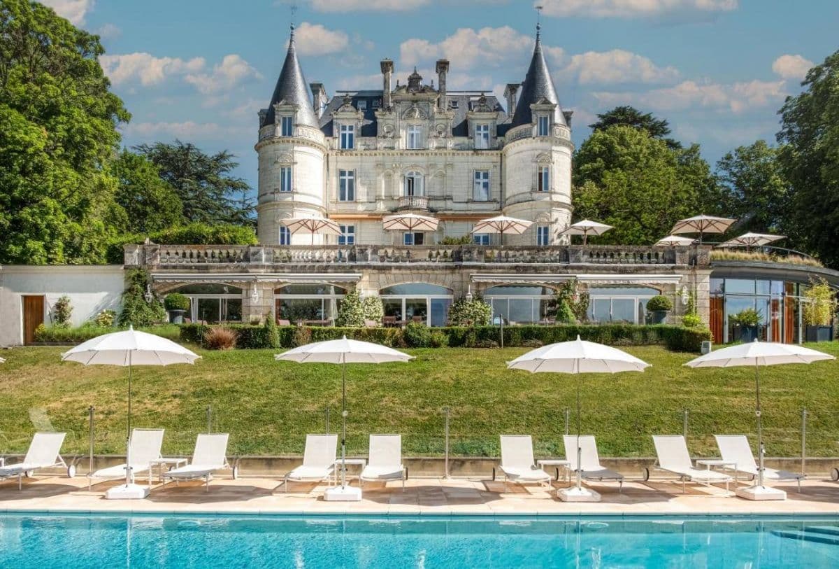 French chateau with outdoor swimming pool, lounge chairs, and umbrellas on a sunny day.