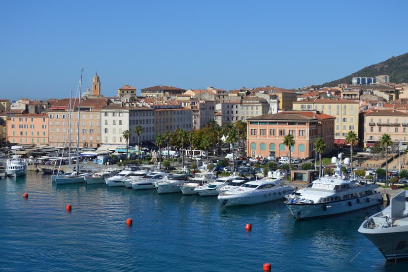 Ajaccio harbour with moored yachts and coastal buildings under clear blue sky