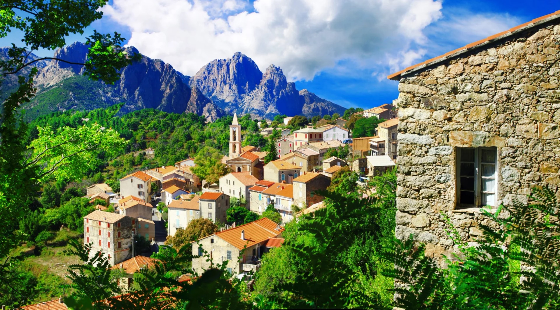 Mountain village in Corte, Corsica, with stone buildings, terracotta roofs, and rugged peaks.