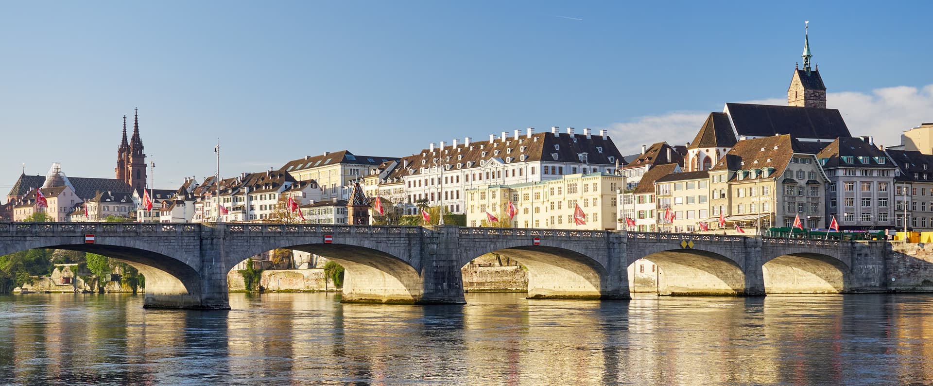 Stone arch bridge over river with historic buildings and church spires in Basel.