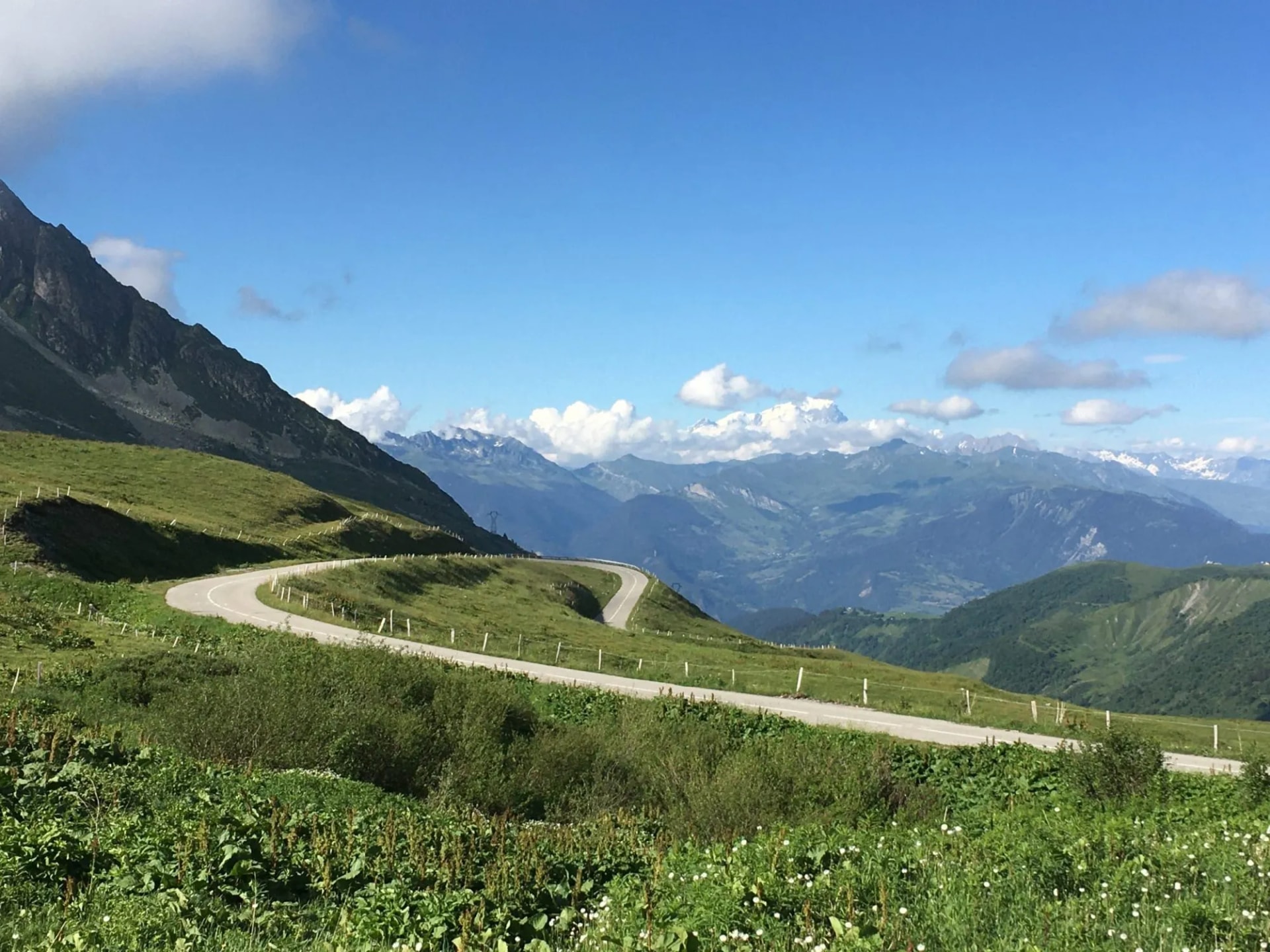 Winding mountain road at Col de la Madeleine in summer with green slopes and blue sky.