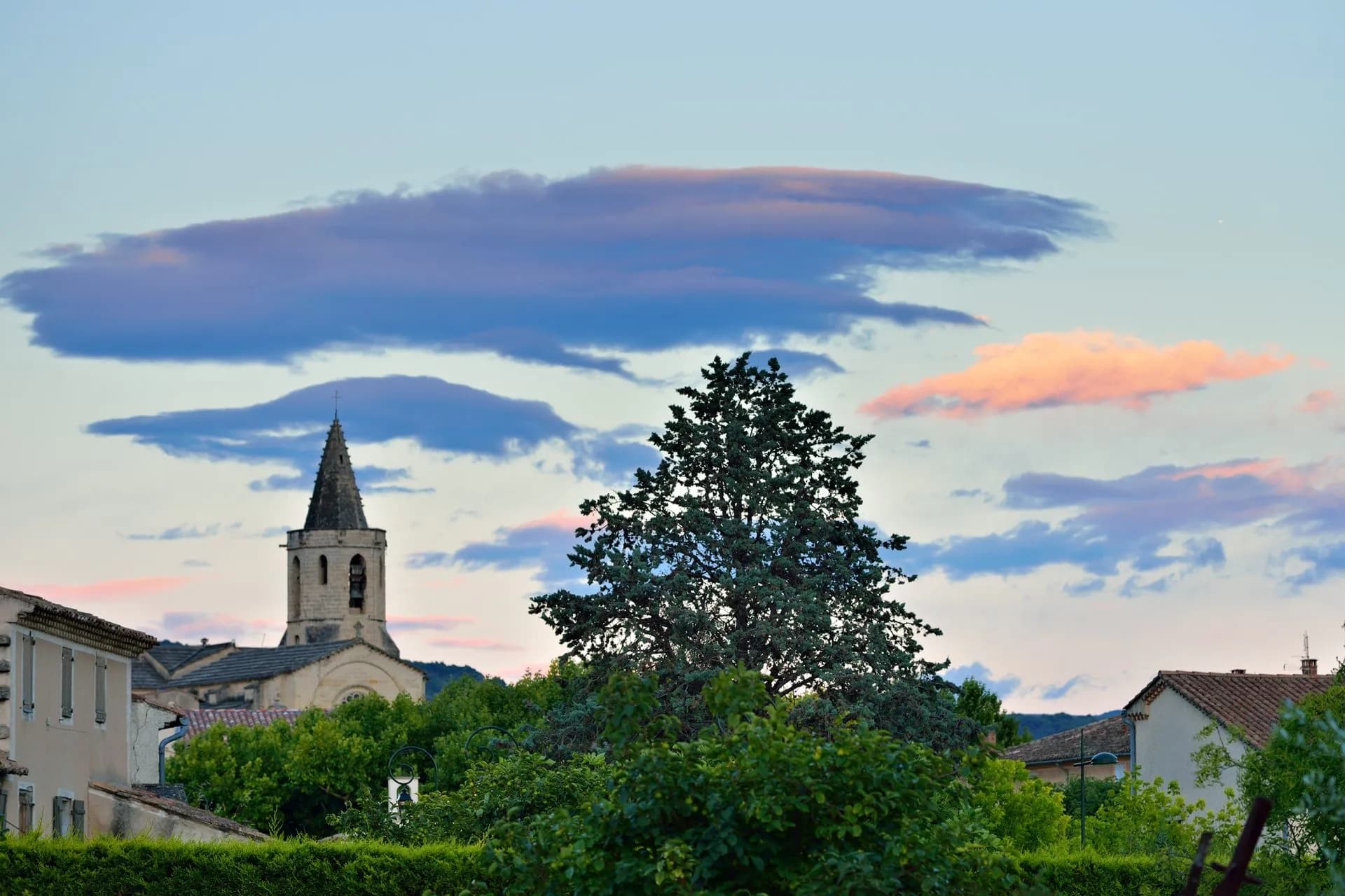 Sunset over the medieval village of Mazan, Provence, France, with a church steeple and tall tree.