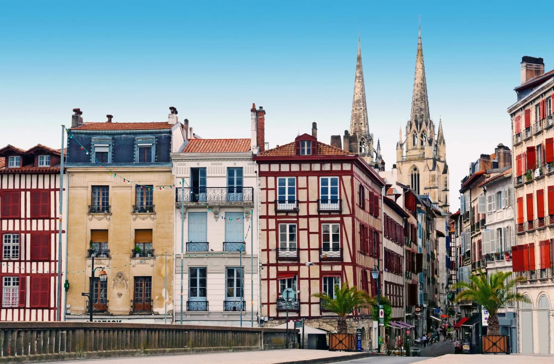 Colorful historic buildings line a street leading to tall cathedral spires under a clear blue sky.