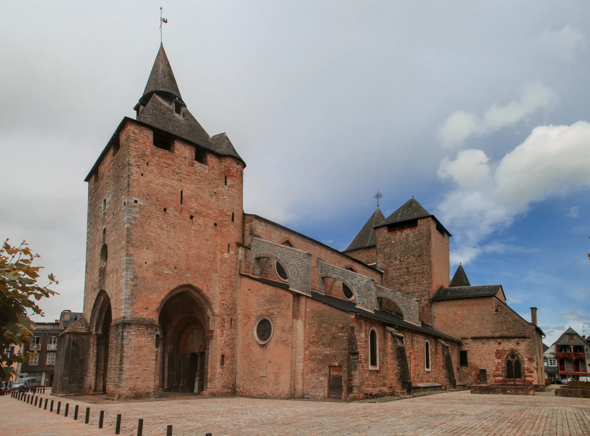 Stone church with Romanesque and Gothic features on a paved square under a cloudy sky.