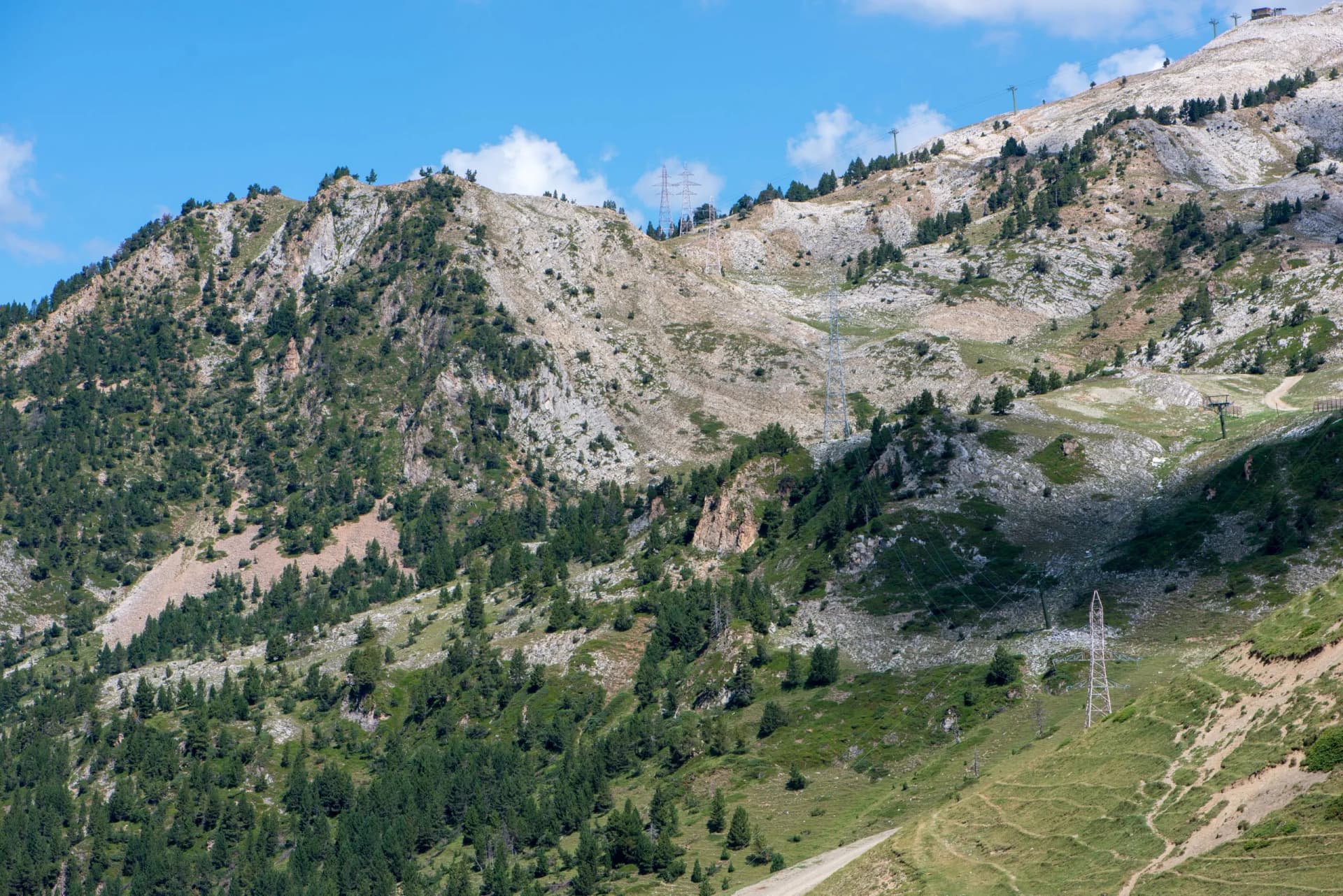 Rocky mountainside in the Aran Valley, Pyrenees, Spain, with scattered pine trees and power lines.