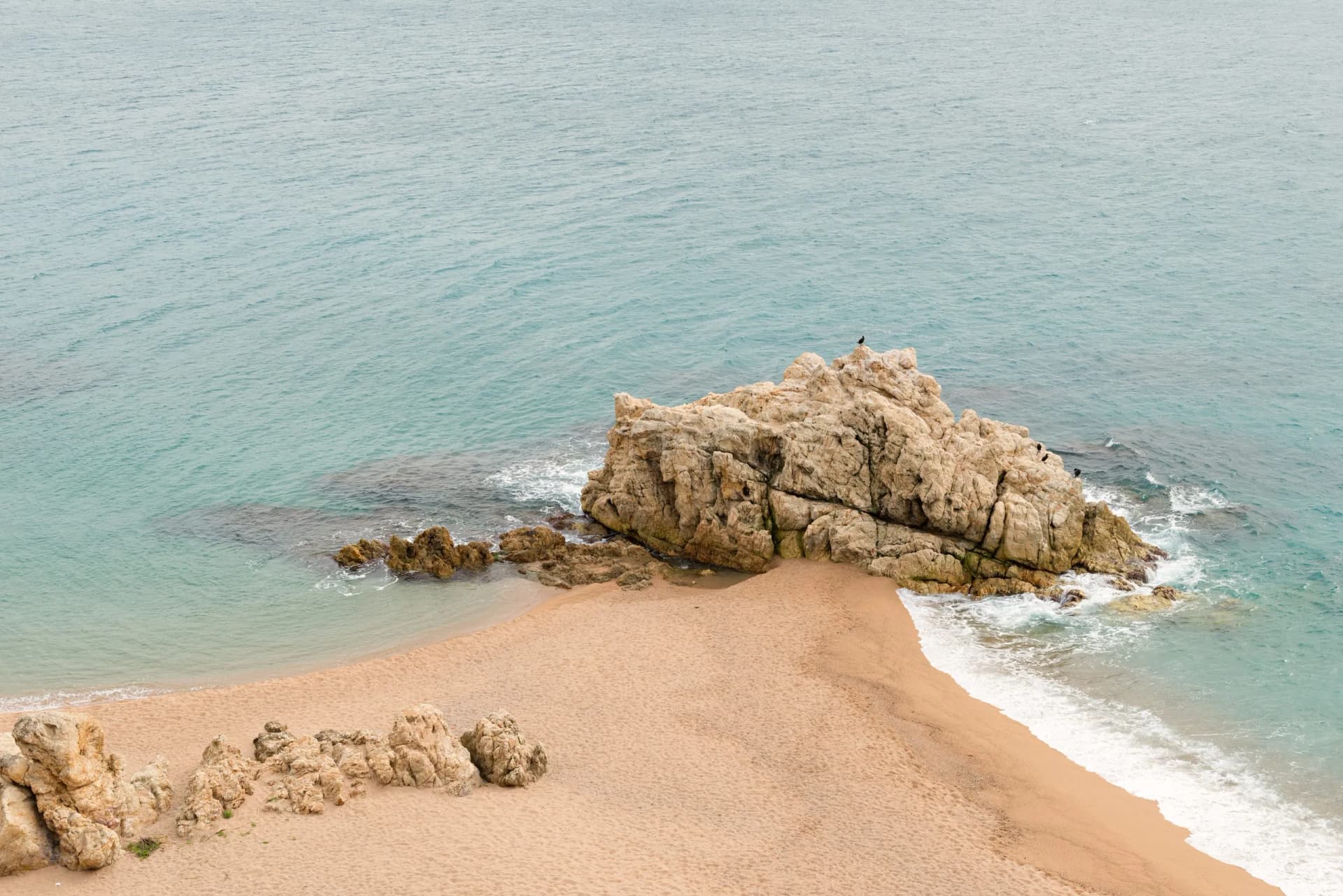 Sandy cove with large rocks jutting into turquoise water, Costa Brava, Girona, Spain.