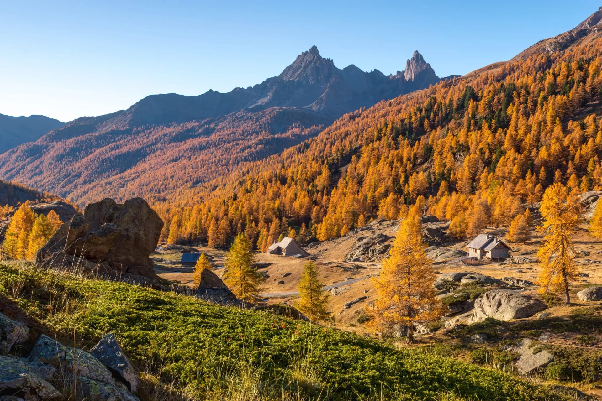 Alpine valley with sharp peaks, golden autumn trees, and small stone huts in the Cerces Massif, Hautes-Alpes.