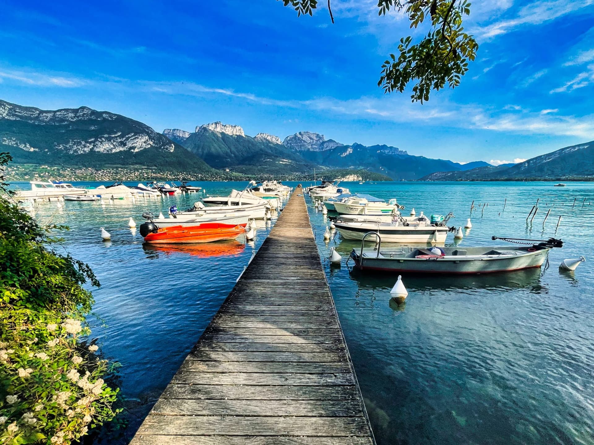 Wooden pier with boats docked on Annecy alpine lake, mountains in background