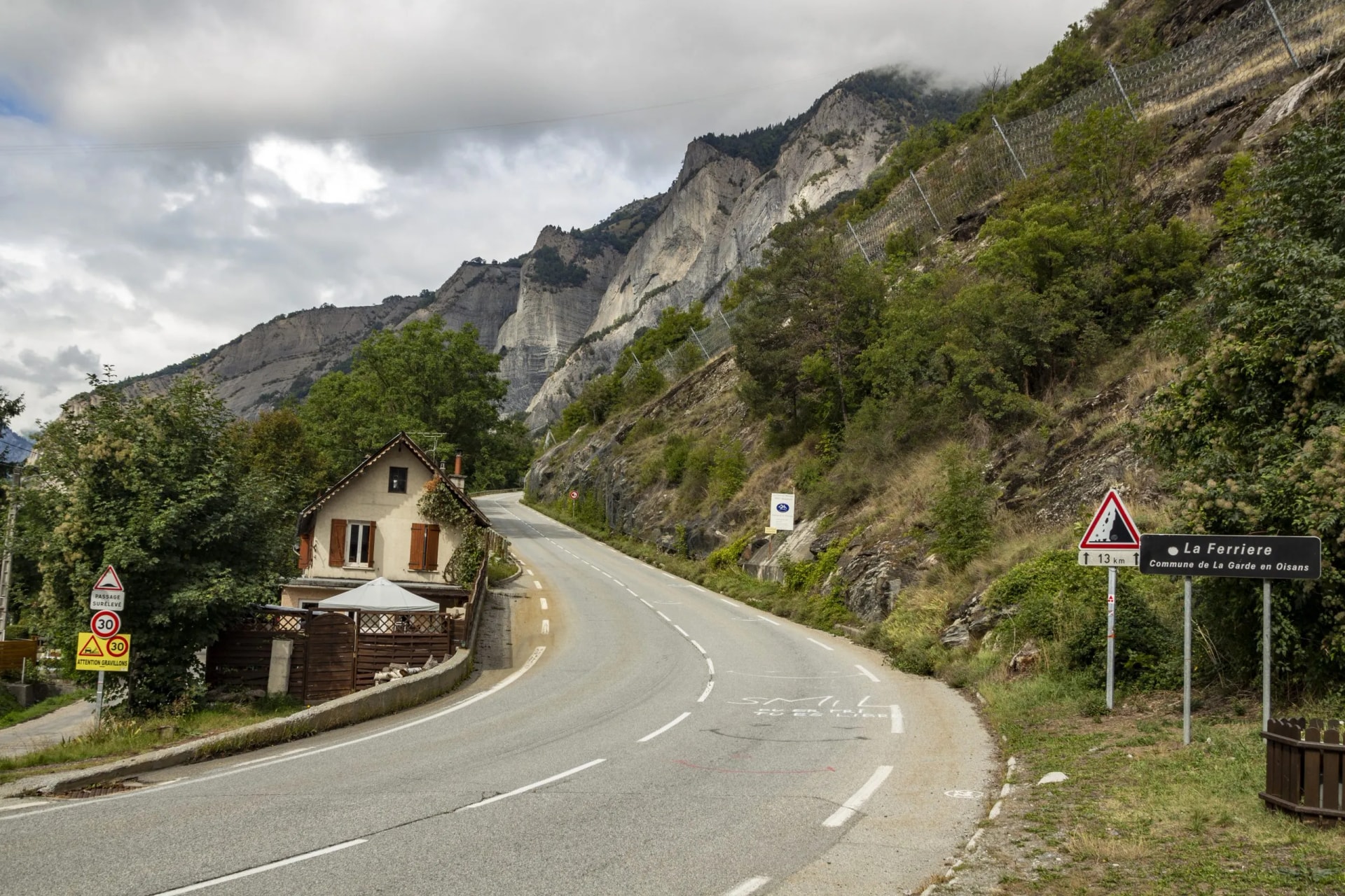 Winding mountain road ascent near La Ferriere, France, with steep cliffs and small house.