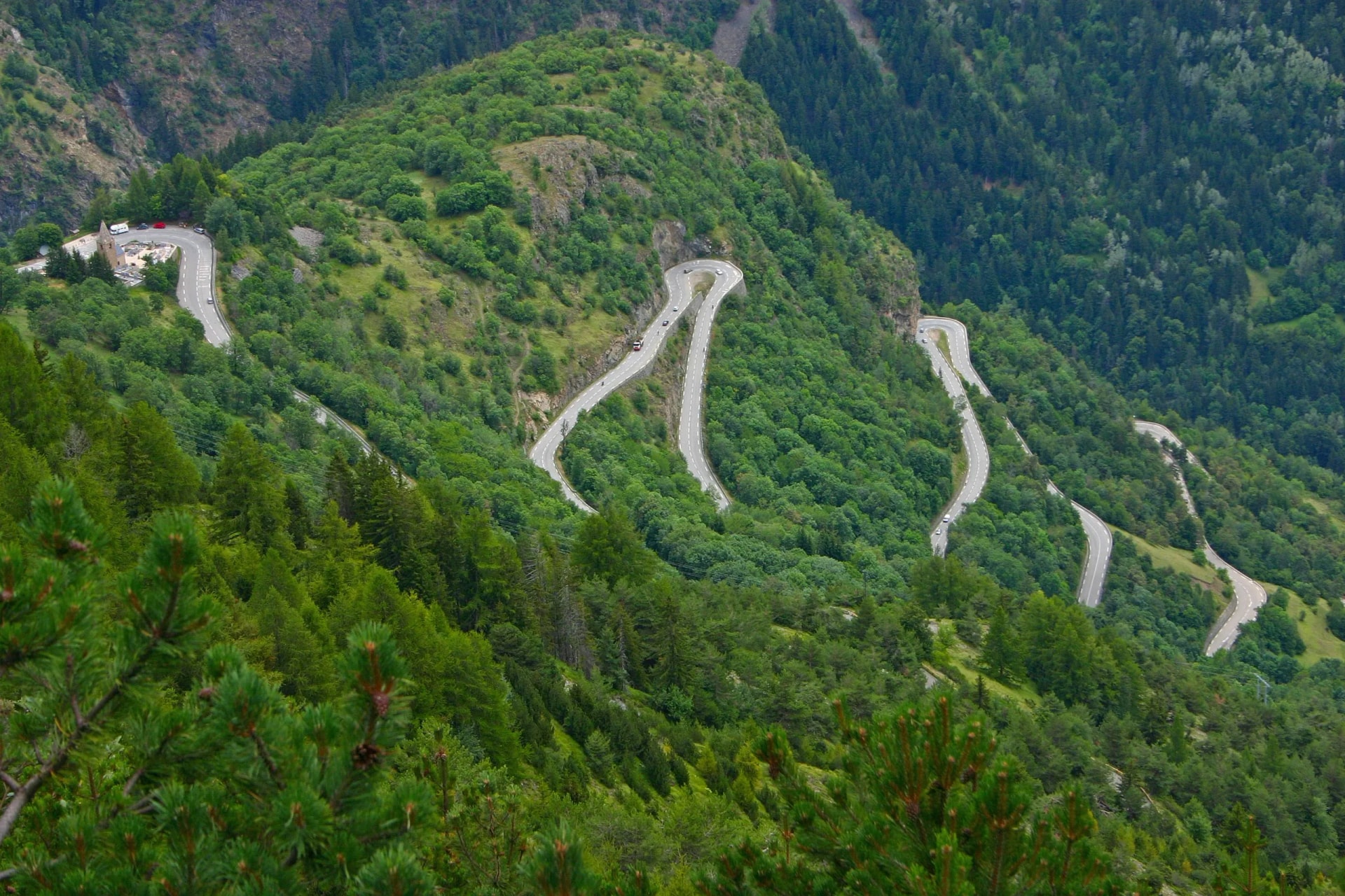 Winding mountain road with hairpin curves through dense green forest, Alpe d'Huez.