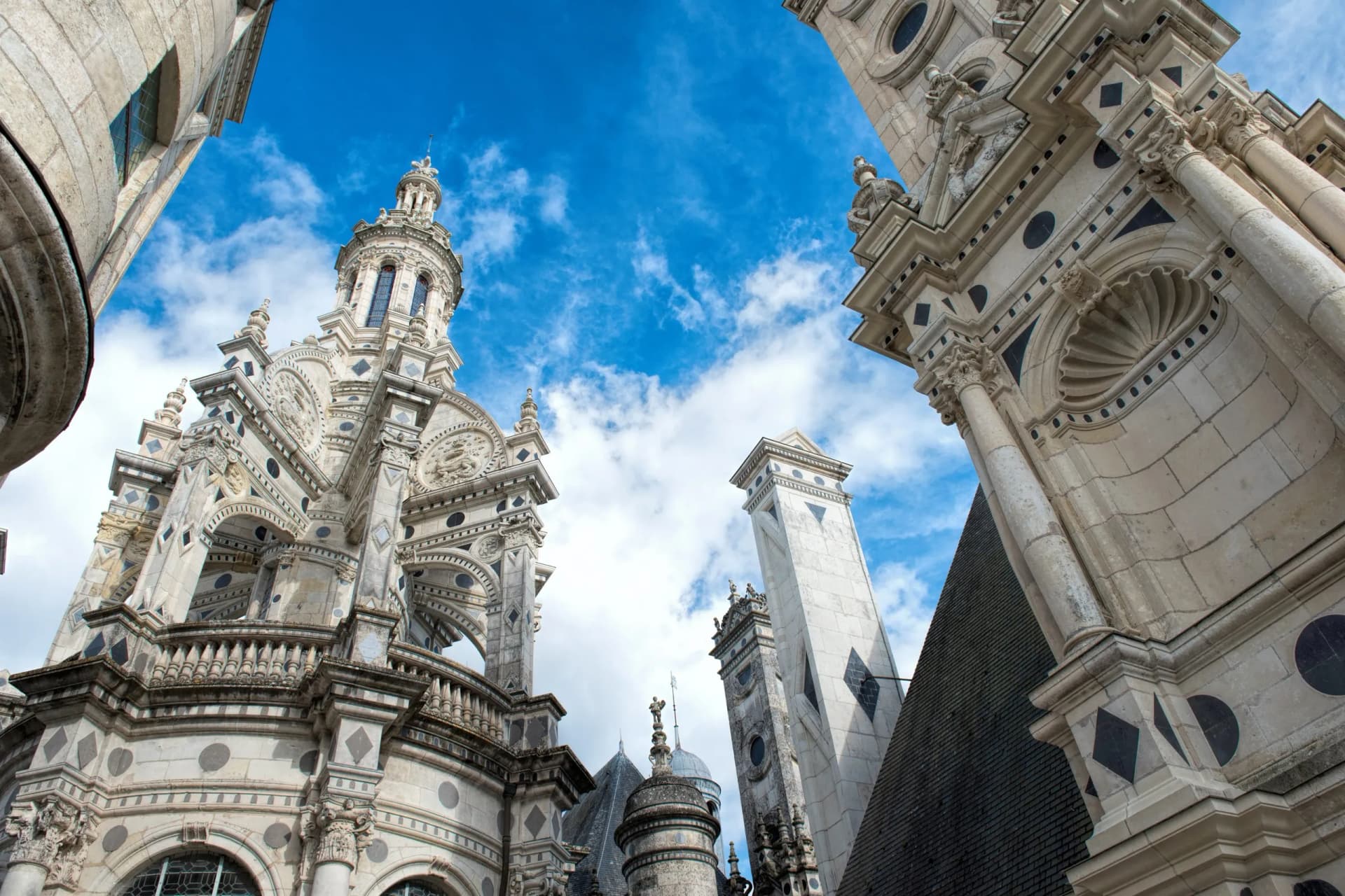 Château de Chambord ornate towers and stonework against a bright blue sky with clouds.