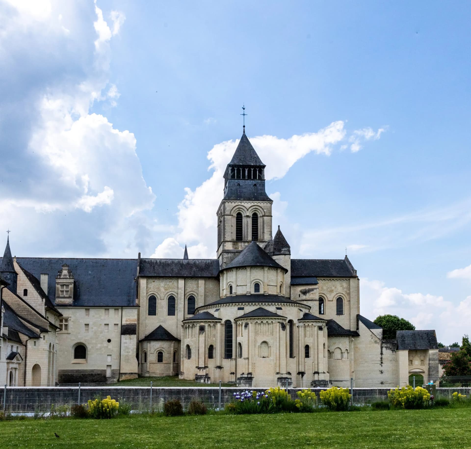 Fonfeveraud Abbey, a large historic stone building with a central tower, under a cloudy blue sky.