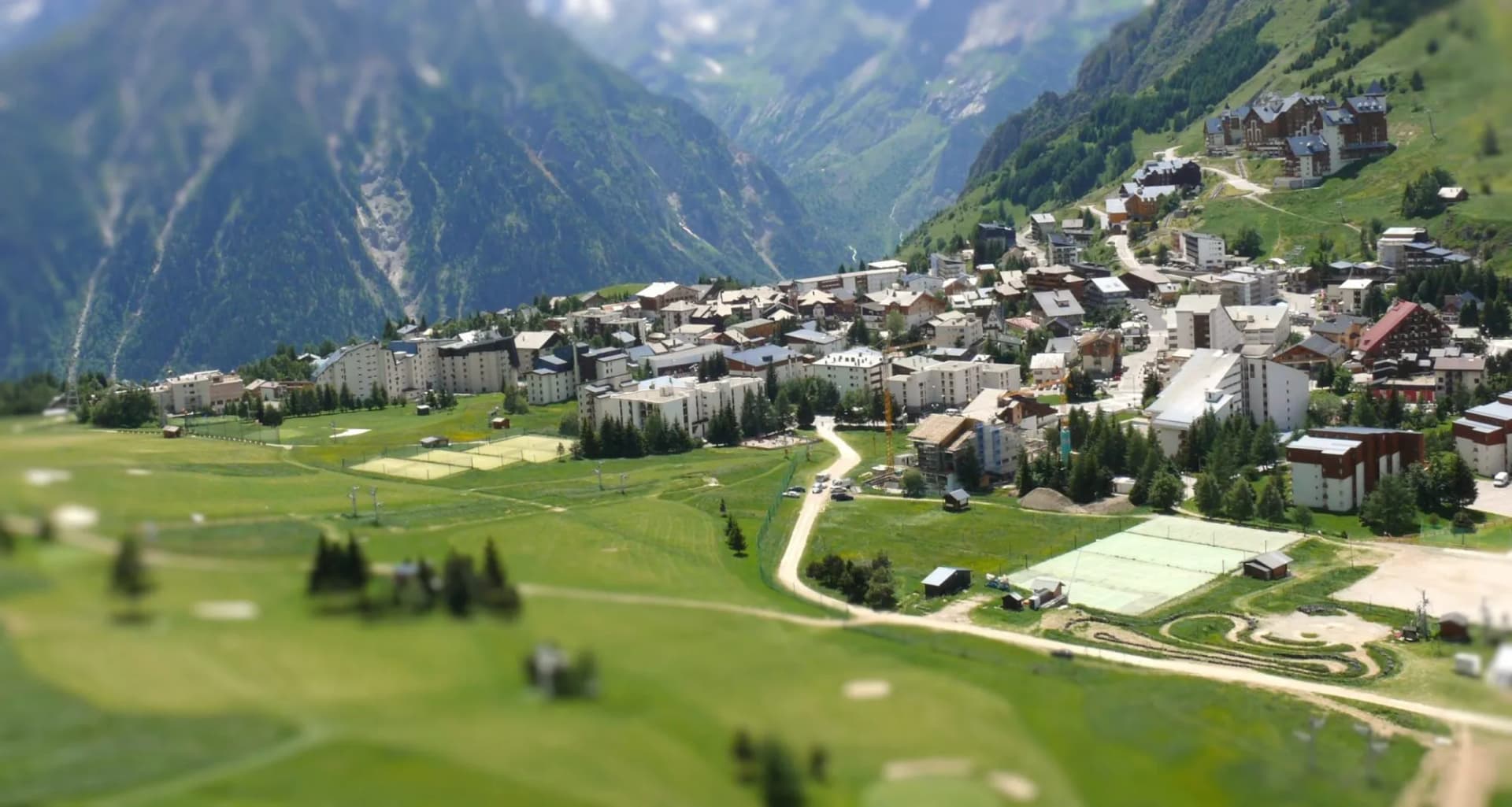 Alpine village with buildings nestled in green mountains during summer season at Les Deux Alpes.
