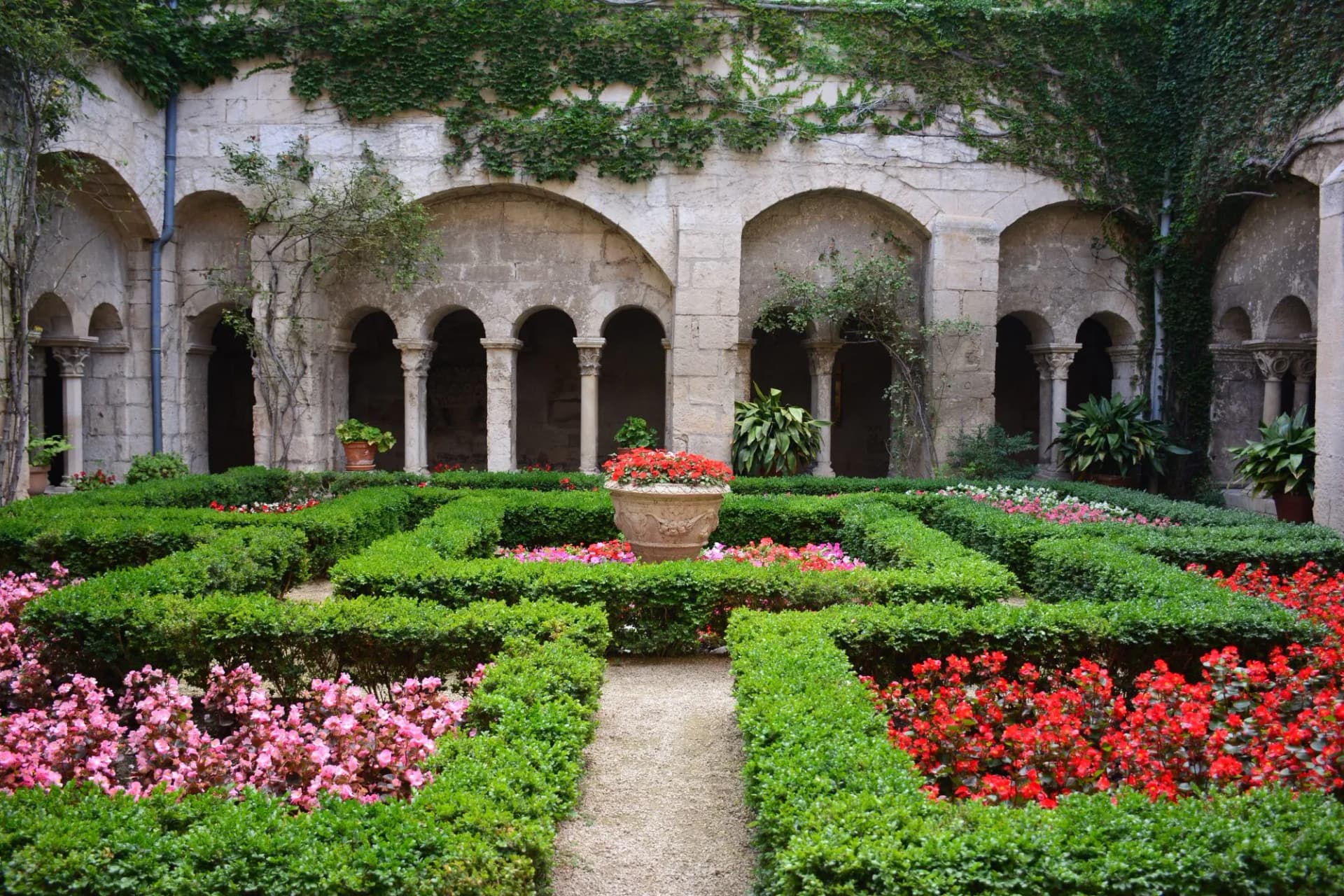 Courtyard garden with manicured hedges, colorful flowers, and stone arches in Saint-Remy de Provence, France.