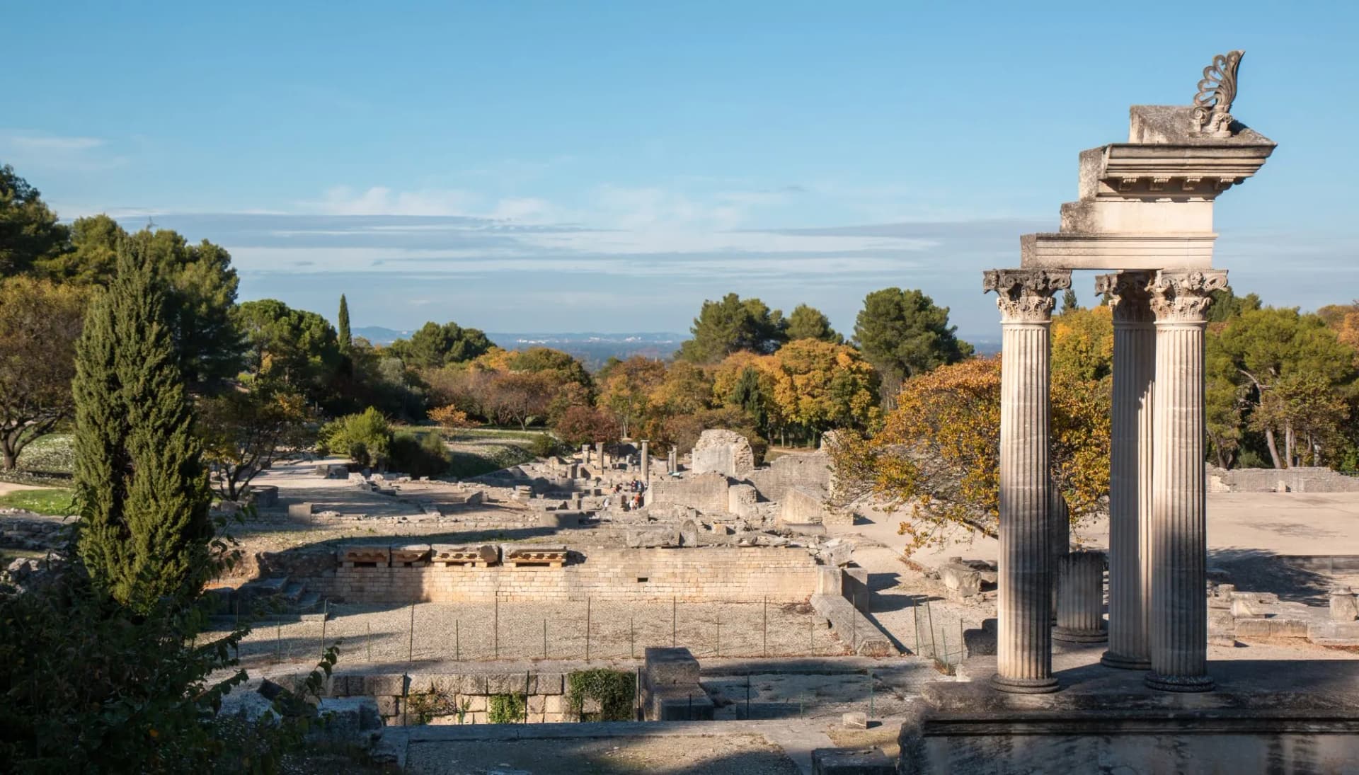 Ruins of Glanum featuring three standing Corinthian columns against a backdrop of trees.