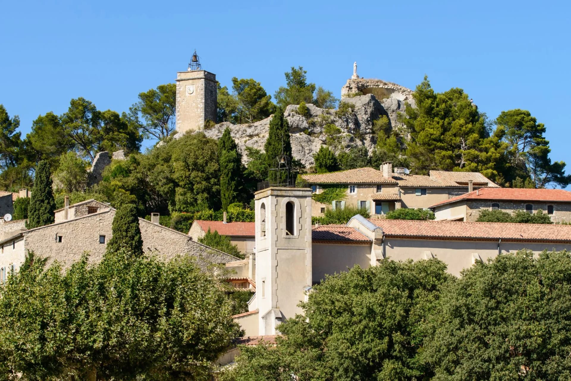 Village buildings with bell tower and clock tower on rocky hill in Eygalières.