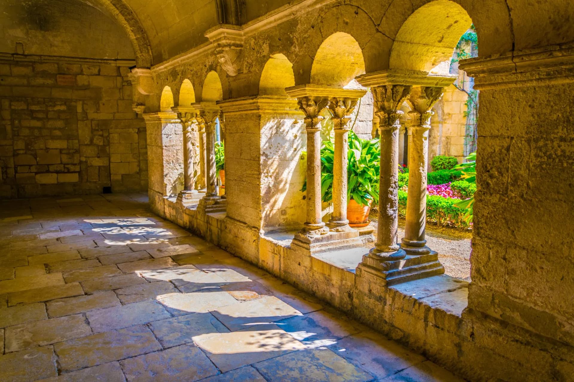 Stone cloister hallway with arched colonnade overlooking a sunny garden at Saint-Paul-de-Mausole.