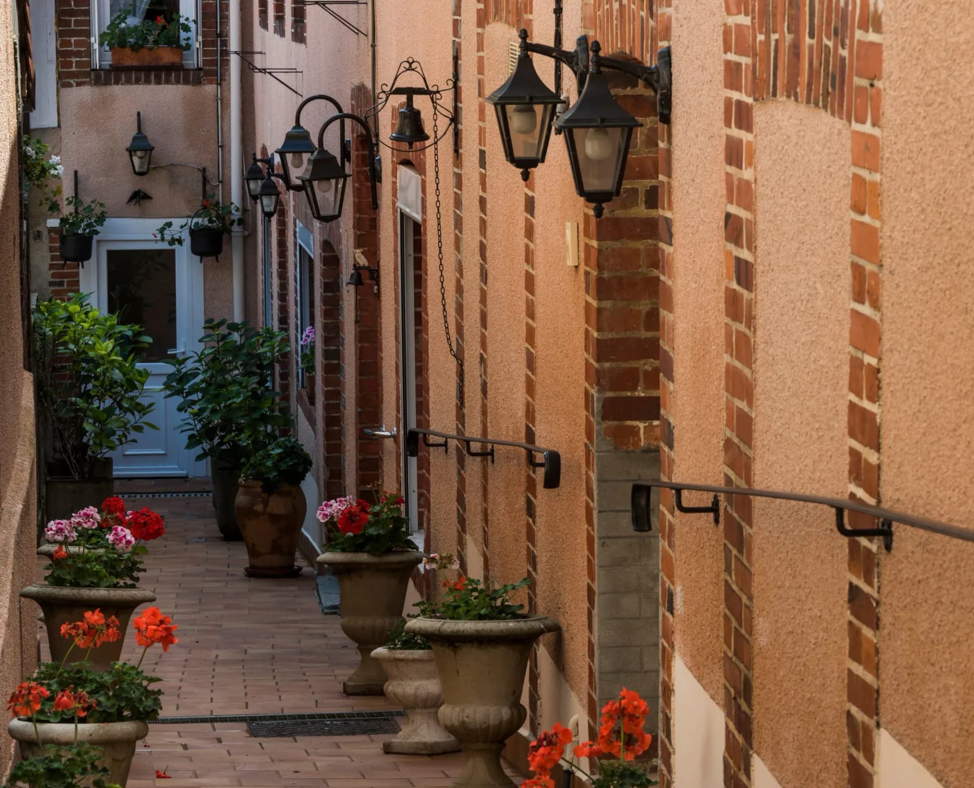 Narrow alleyway with potted geraniums, ornate lanterns, and brick accents in Hautvillers.