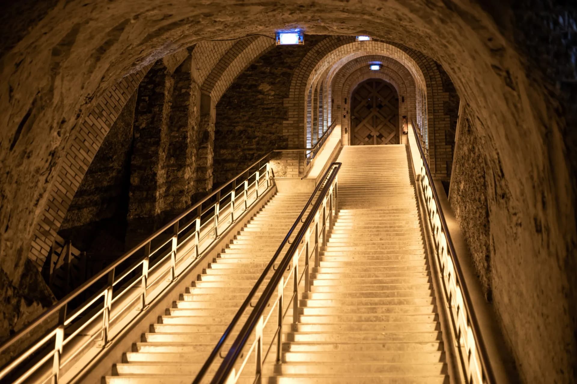 Illuminated stone staircase ascending into a vaulted cellar tunnel in Reims.