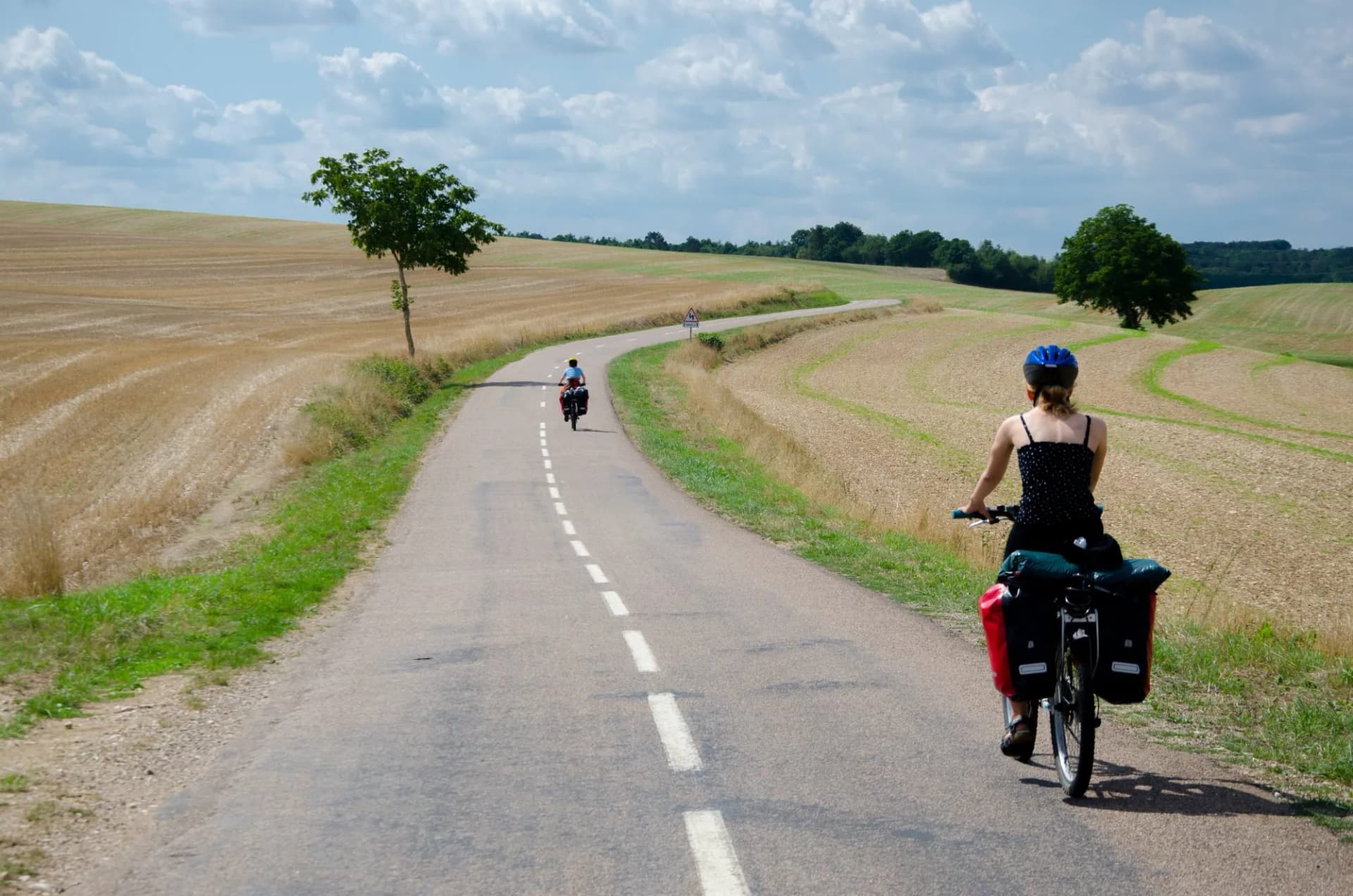 Cyclists touring on a paved road through harvested fields under a cloudy sky, Burgundy.