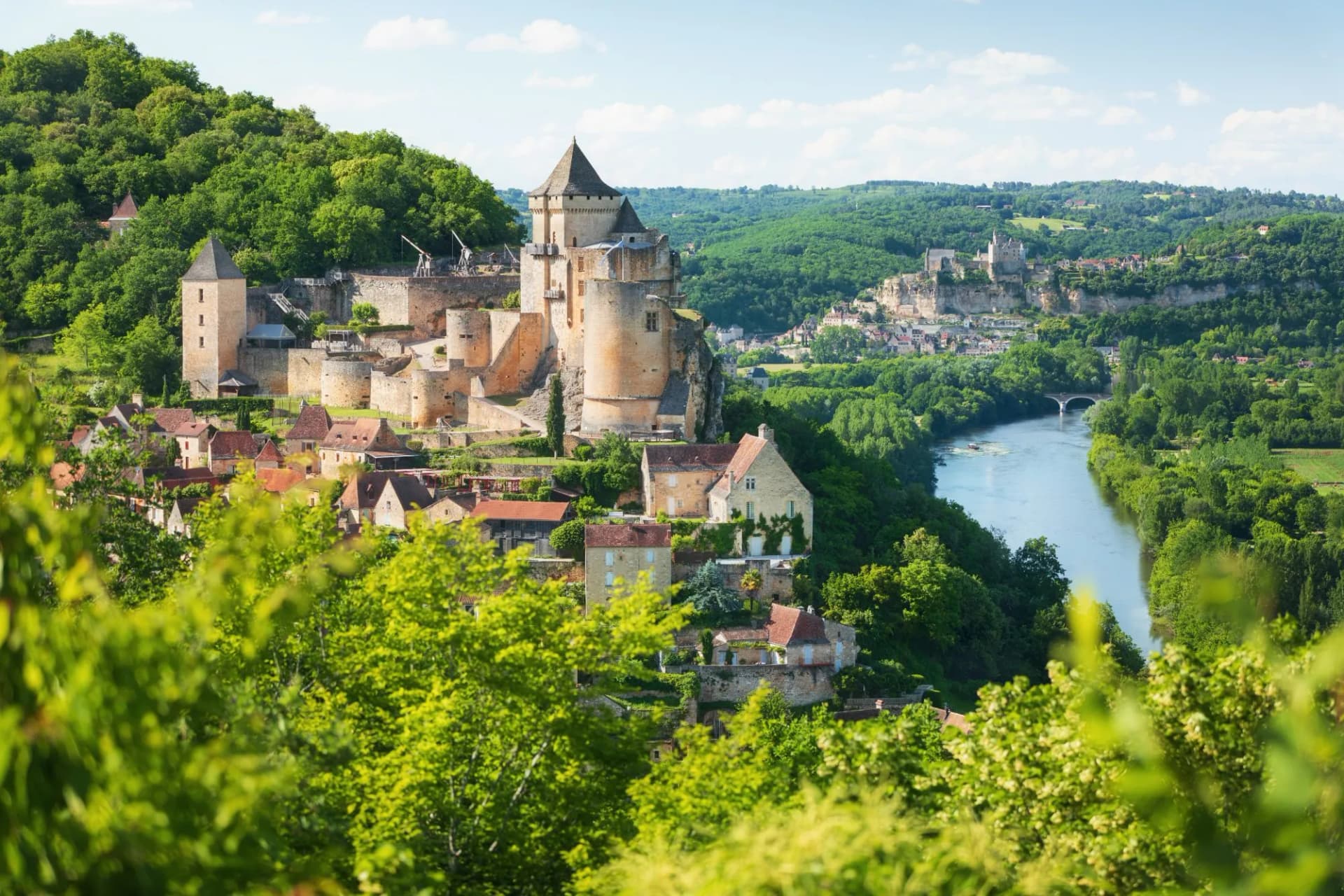 Medieval castle overlooking a village, river, and lush green hills in the Dordogne Valley.