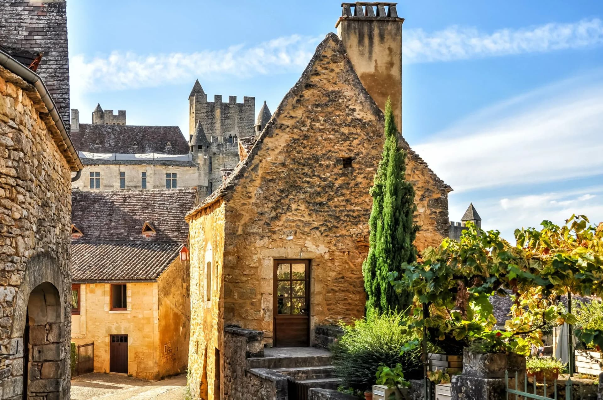 Stone buildings and castle towers in a narrow street in the Dordogne countryside.