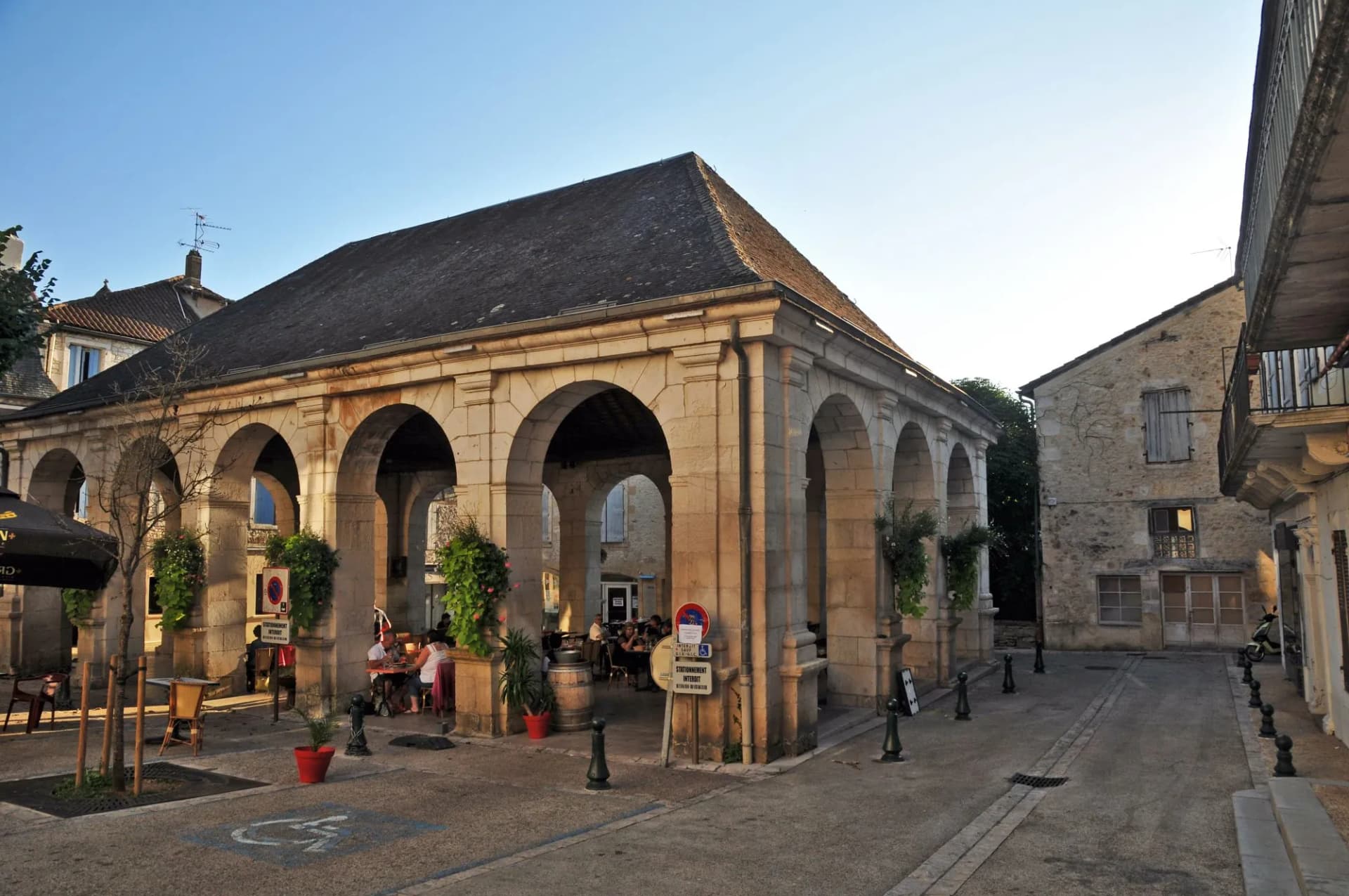 Covered market hall with stone arches and outdoor dining in Souillac on a clear day.