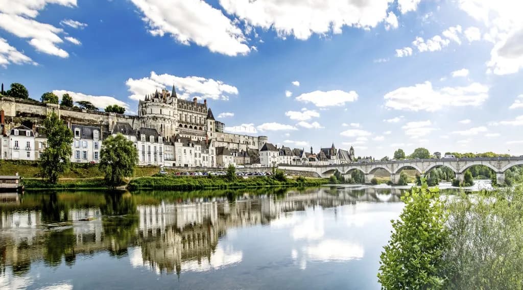 Panorama of Amboise town with the château, river, and bridge under a blue, cloudy sky.