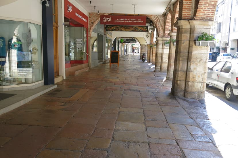 Stone arcades and storefronts along a cobblestone walkway in Louhans