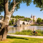 Avignon, Frankrig - 16. maj 2018: Folk cykler eller hviler sig på en solrig dag på bredden af Rhône, overfor Saint-Benezet-broen, også kendt som Avignon-broen, og det pavelige palads.