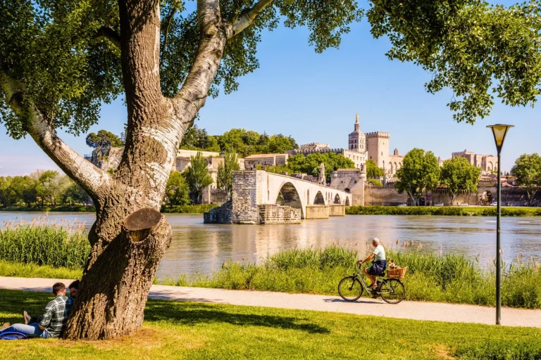Avignon, Frankreich - 16. Mai 2018: Menschen radeln oder ruhen sich an einem sonnigen Tag am Ufer der Rhone aus, gegenüber der Saint-Benezet-Brücke, auch bekannt als Avignon-Brücke, und dem Papstpalast.