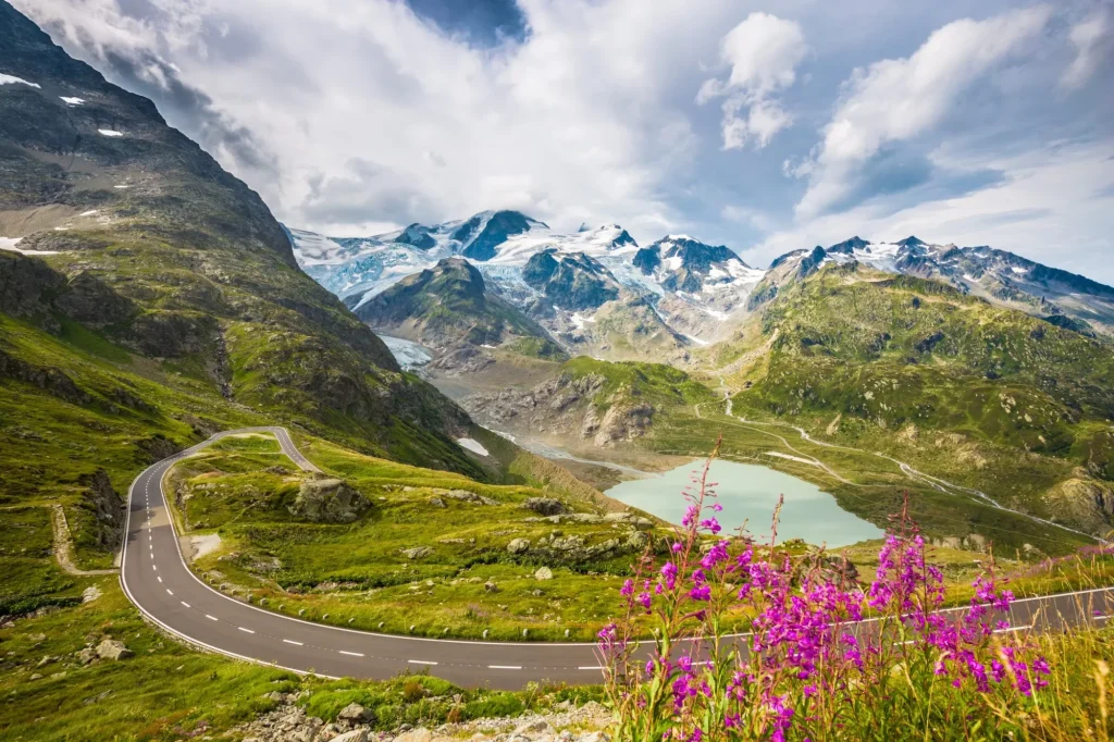 Beautiful view of winding mountain pass road in the Alps running through idyllic alpine scenery with mountain peaks, glaciers, lakes and green pastures with blooming flowers in summer
