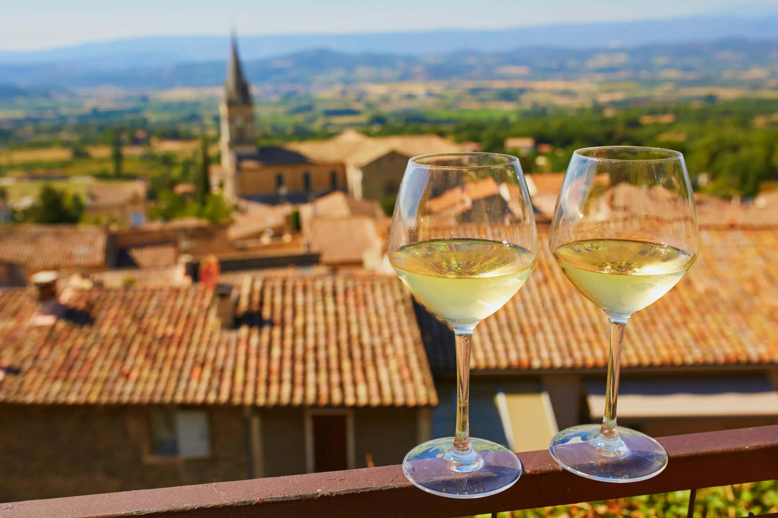 Two glasses of white wine with view to beautiful old roofs of Bonnieux village in Provence, France